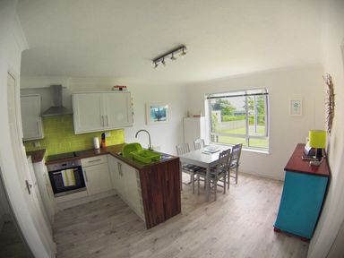 A kitchen and dining area with white cabinets green tile backsplash a white table and chairs next to a window at Driftwood in Bude