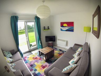 A living room with two grey sofas a colorful rug a small wooden coffee table and a television at Driftwood in Bude