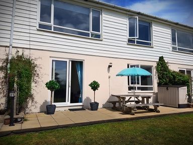 A patio with a picnic table and umbrella outside a two-story house at Driftwood in Bude