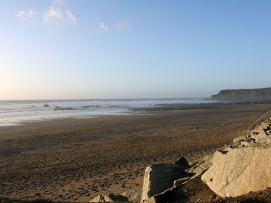 A sandy beach with rocks, ocean waves, and a cliff in the distance at Driftwood in Bude