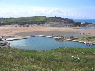 A coastal scene with a tidal pool in the foreground a sandy beach and rocky cliffs in the background at Driftwood in Bude