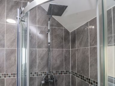 A shower with a glass enclosure and tiled walls at Coetsiws in Clynnog Fawr