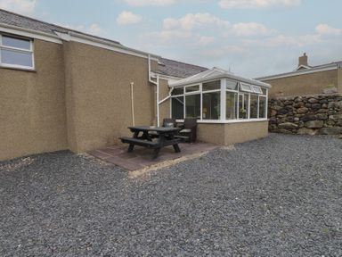 A garden with a conservatory and dining table at Coetsiws in Clynnog Fawr