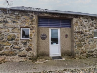 The entrance of a stone building with windows and a sign at Coetsiws Clynnog Fawr