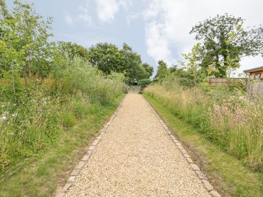 A gravel pathway bordered by grass and shrubs leading to a wooden gate in a garden at Tickencote in Exton Rutland