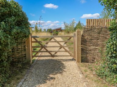 A wooden gate opening to a gravel pathway with woven and wooden fences and greenery at Tickencote in Exton Rutland
