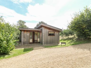 A wooden house with a gravel driveway and surrounding trees at Tickencote in Exton Rutland