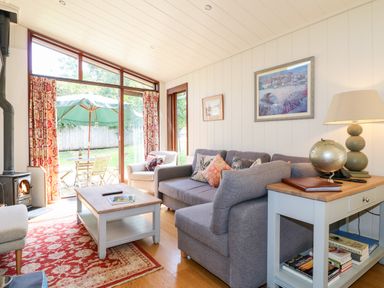 A living room with a gray sofa white armchair wooden coffee table and glass doors leading to a patio at Tickencote in Exton Rutland