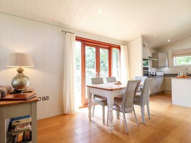 A dining area with a wooden table and chairs next to glass doors and a kitchen with cabinets and appliances at Tickencote in Exton Rutland