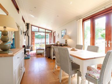 A dining area with a wooden table and chairs next to large wooden framed glass doors and a living area with a sofa and coffee table near a wood burning stove at Tickencote in Exton Rutland