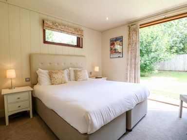 A bedroom with a large bed two bedside tables with lamps a window and a sliding door showing a garden at Tickencote in Exton Rutland