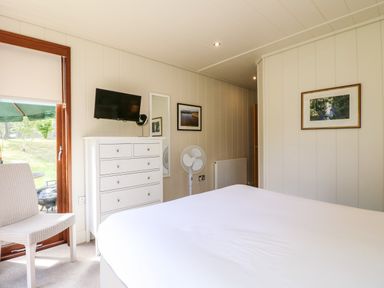 A bedroom with a bed white chest of drawers chair fan and framed pictures at Tickencote in Exton Rutland
