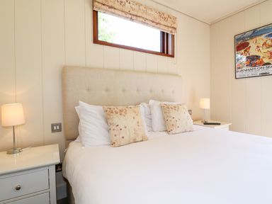 A bedroom with a large bed with floral pillows bedside tables with lamps and a wall framed poster at Tickencote in Exton Rutland