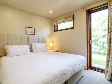 A bedroom with a double bed white pillows a bedside table with a lamp and a glass door leading outside at Tickencote in Exton Rutland
