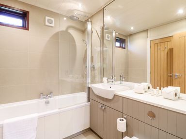 A bathroom with a bathtub shower combination a sink with countertop and mirror and wooden door at Tickencote in Exton Rutland
