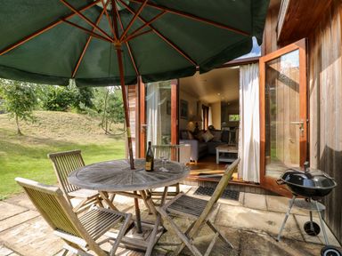 A patio with a round wooden table and four chairs under a green umbrella next to an open door leading to a living room at Tickencote in Exton Rutland