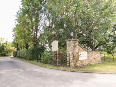 A driveway with a stone wall and sign for Barnsdale surrounded by trees and grass at Tickencote Exton Rutland