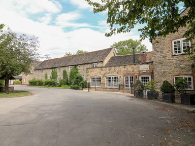 A stone building with a reception sign and potted plants along a curved driveway at Tickencote in Exton Rutland