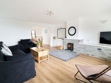 A living room with a black sofa armchair wooden coffee table stone fireplace and dining area at Seal Cottage in Mortehoe