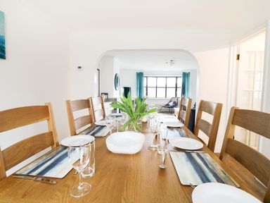 A dining room with a wooden table and chairs set with plates glasses and placemats at Seal Cottage in Mortehoe