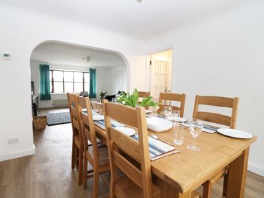 A dining room with a wooden table and chairs set with plates glasses and a flower vase at Seal Cottage in Mortehoe