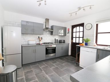 A kitchen with grey cabinets white tiled backsplash and appliances at Seal Cottage in Mortehoe
