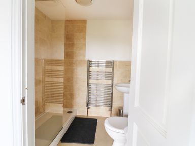 A bathroom with a shower, a towel radiator, a sink, a toilet, and a dark bath mat at Seal Cottage in Mortehoe