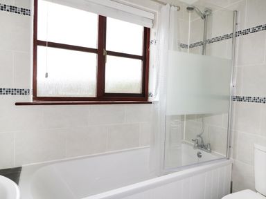 A bathroom with a bathtub shower combination and a window above the tub at Seal Cottage in Mortehoe