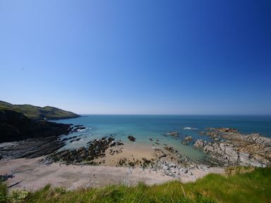 A rocky beach with sand and grassy hills by the sea at Seal Cottage in Mortehoe