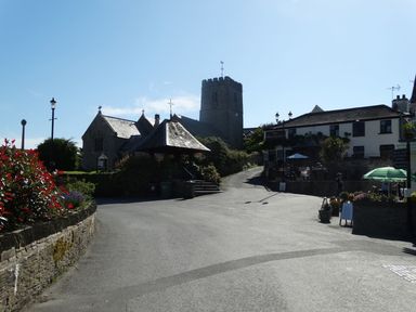 A village street with a church, a stone shelter, flowers, and a building with outdoor seating at Seal Cottage in Mortehoe