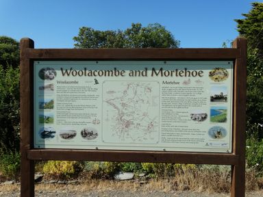 An informational wooden board about Woolacombe and Mortehoe with text images and a map outdoors