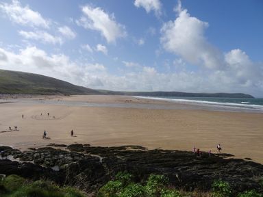 A wide sandy beach with people walking and playing near rocky formations under a blue sky at Seal Cottage in Mortehoe