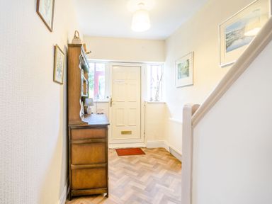 A hallway with a wooden cabinet a white door framed pictures and a staircase at The Perks in Scarborough