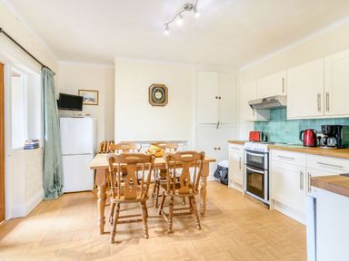 A kitchen with wooden dining table and chairs a refrigerator a stove and white cabinets at The Perks in Scarborough