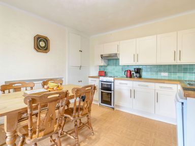 A kitchen with wooden dining table and chairs white cabinets and blue tiled backsplash at The Perks in Scarborough