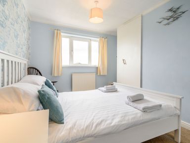A bedroom with a white bed and folded towels on it next to a window with light curtains at The Perks in Scarborough