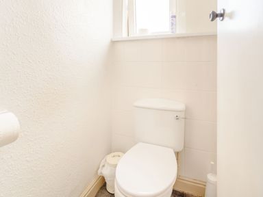 A small bathroom with a white toilet a trash bin window and an open door at The Perks in Scarborough