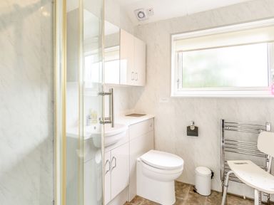 A bathroom with a shower enclosure, toilet, sink with cabinets, window, a small bin, towel rack, and a white chair at The Perks in Scarborough