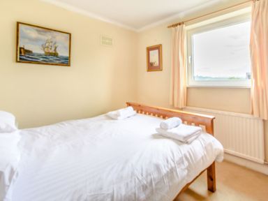 A bedroom with a wooden bed, white bedding, folded towels, a window with curtains, and paintings on the walls at The Perks in Scarborough