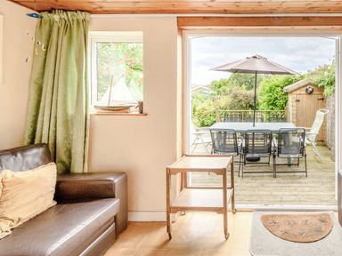 An indoor seating area with a leather sofa and a small wooden cart looking out to a deck with a table and chairs under an umbrella at The Perks in Scarborough