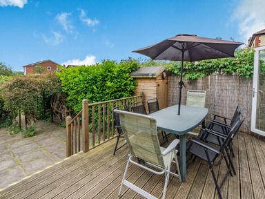 A patio with an outdoor dining table, six chairs, an umbrella, a wooden shed, and greenery at The Perks in Scarborough