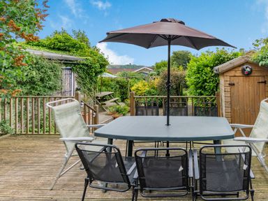 An outdoor wooden deck with a table and chairs and an umbrella surrounded by greenery at The Perks in Scarborough