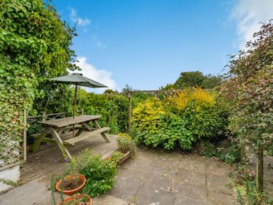 A garden patio with a wooden picnic table and umbrella surrounded by plants and shrubs at The Perks in Scarborough