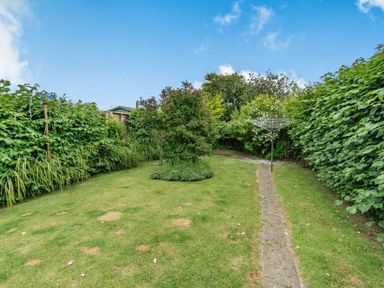 A garden with a grassy lawn a stone path a rotary clothesline and trees at The Perks in Scarborough