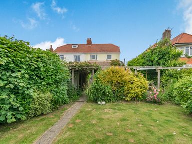 A backyard garden with grass a stone path shrubs bushes and a wooden pergola at The Perks in Scarborough