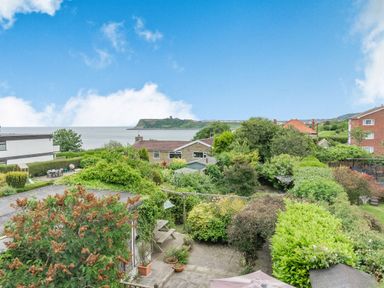 A backyard with bushes a table with chairs and houses in the distance by the sea at The Perks in Scarborough