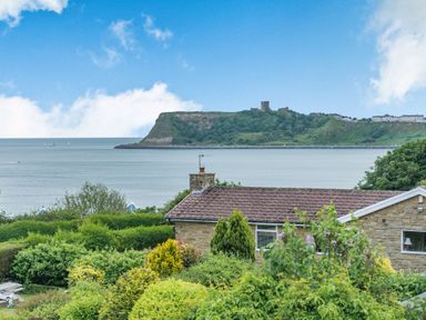 A view of a sea with a headland and buildings behind a house and garden at The Perks in Scarborough