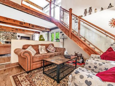 A sitting area with a brown sofa, patterned armchairs, a wooden coffee table, and wooden stairs with glass panels at Eden Mill Millers Beck in Kendal