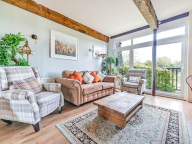 A living room with plaid armchairs a brown sofa wooden coffee table and large windows at Eden Mill Millers Beck in Kendal