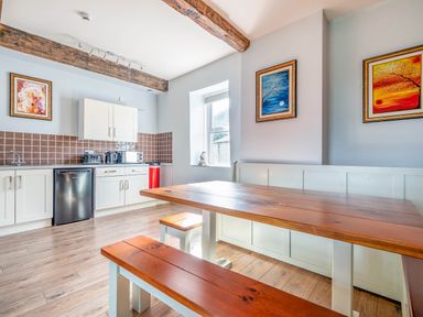 A kitchen with wooden dining table and benches brown tiled backsplash and white cabinets at Eden Mill Millers Beck in Kendal